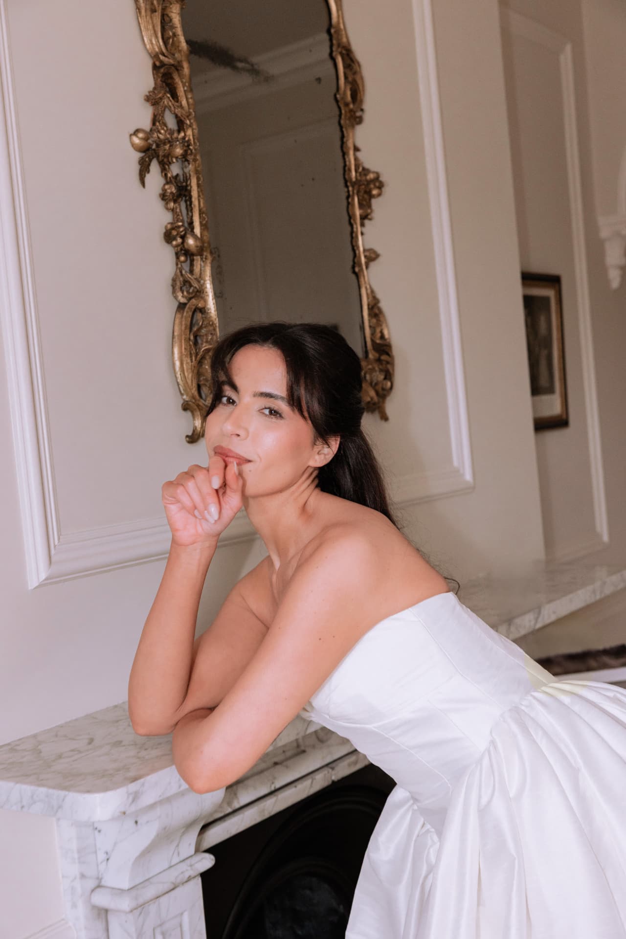 Bride leaning on a marble mantelpiece beneath a gilt mirror.
