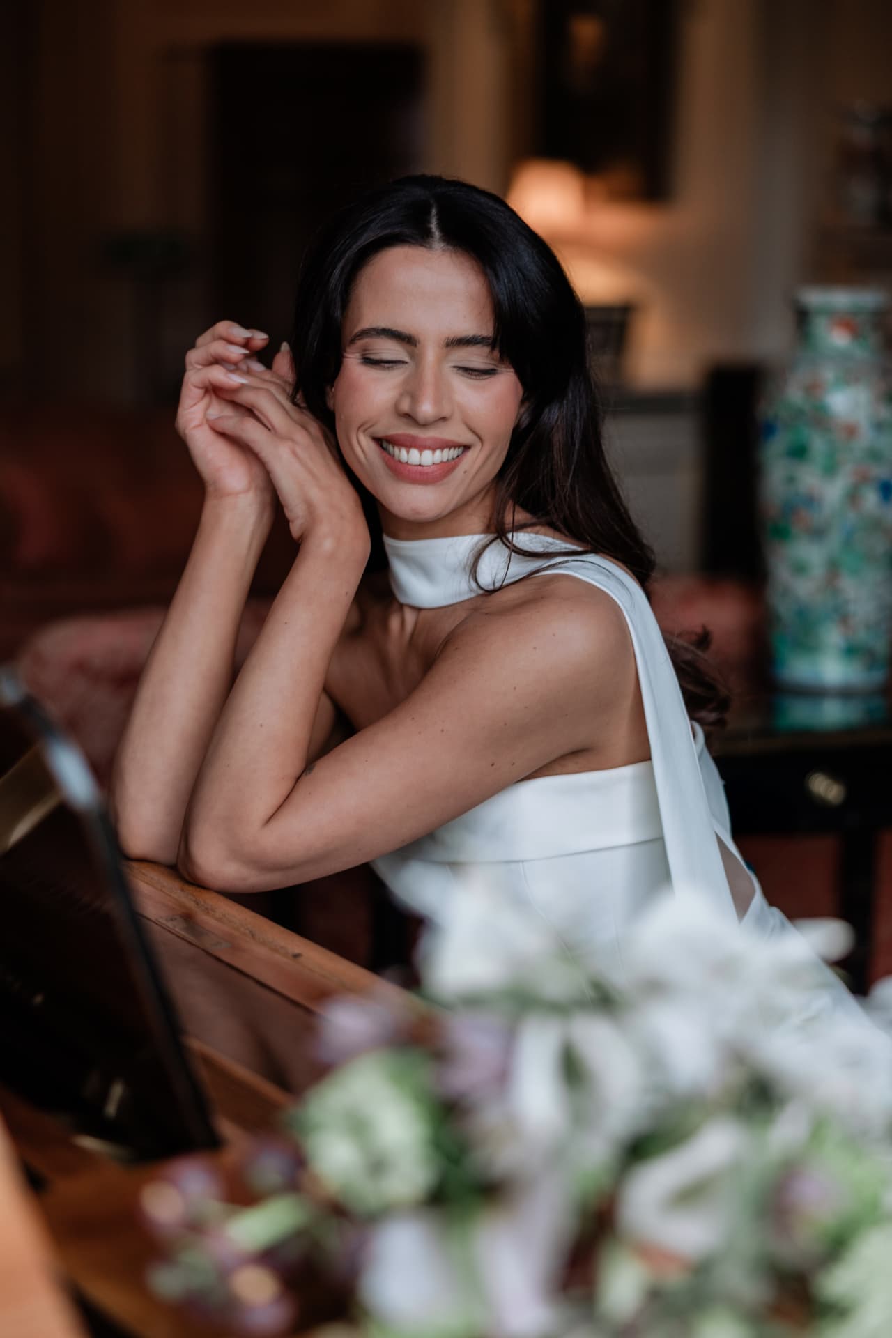 Bride laughing with her eyes closed, hand raised to her hair.