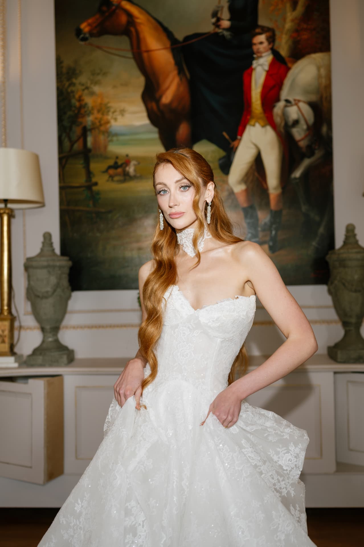 Bride with long copper waves in a lace ballgown and pearl earrings, photographed indoors.