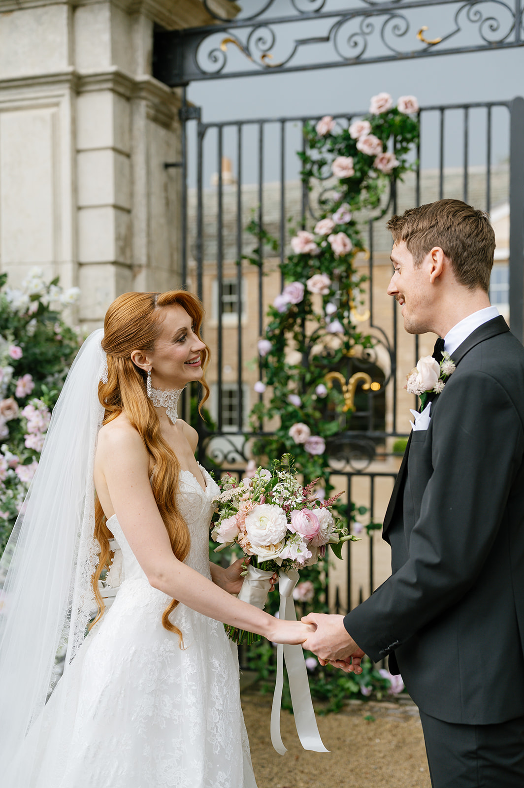 Bride and groom holding hands in front of a flower-dressed iron gate.