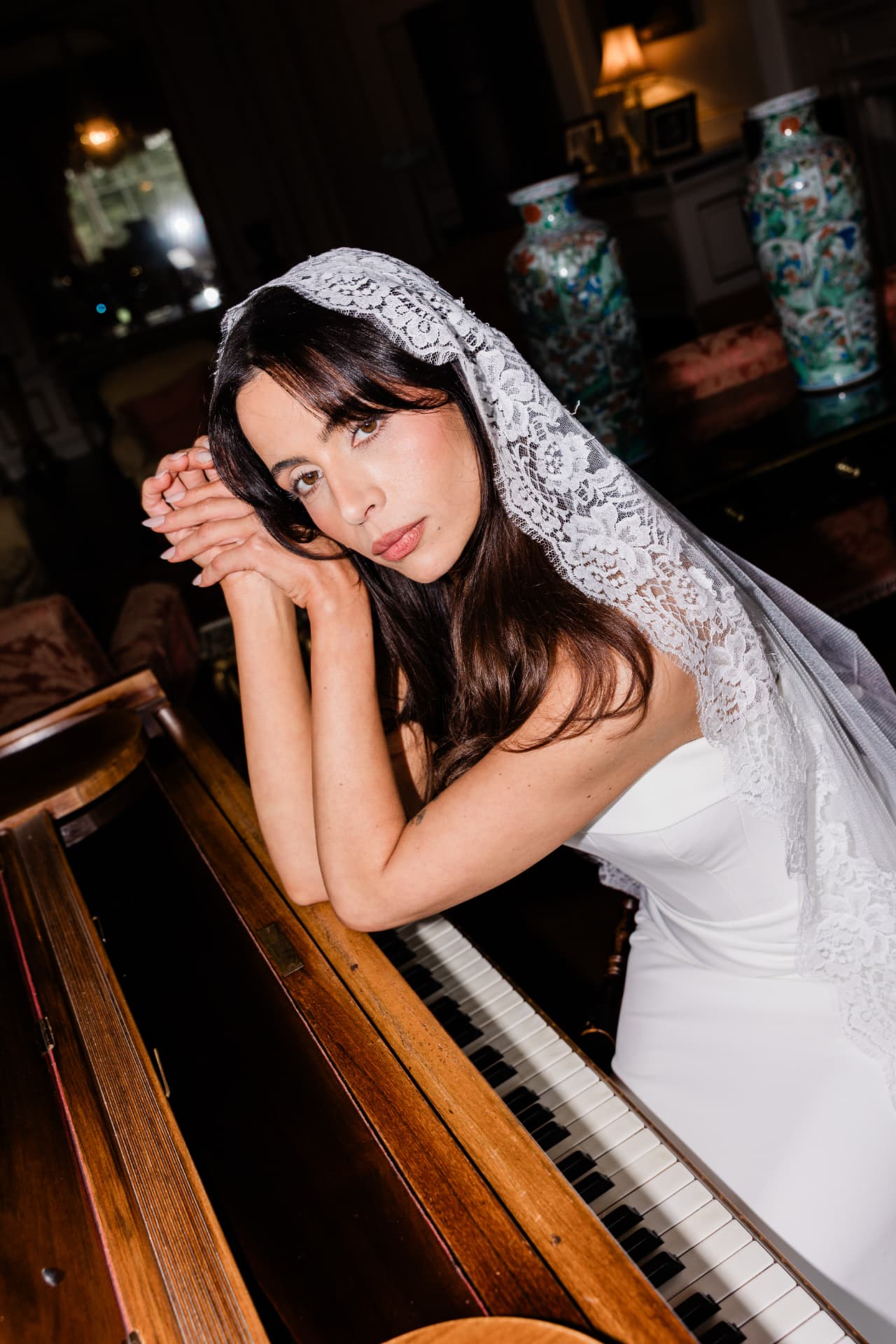 Bride in a lace mantilla veil resting against a grand piano.