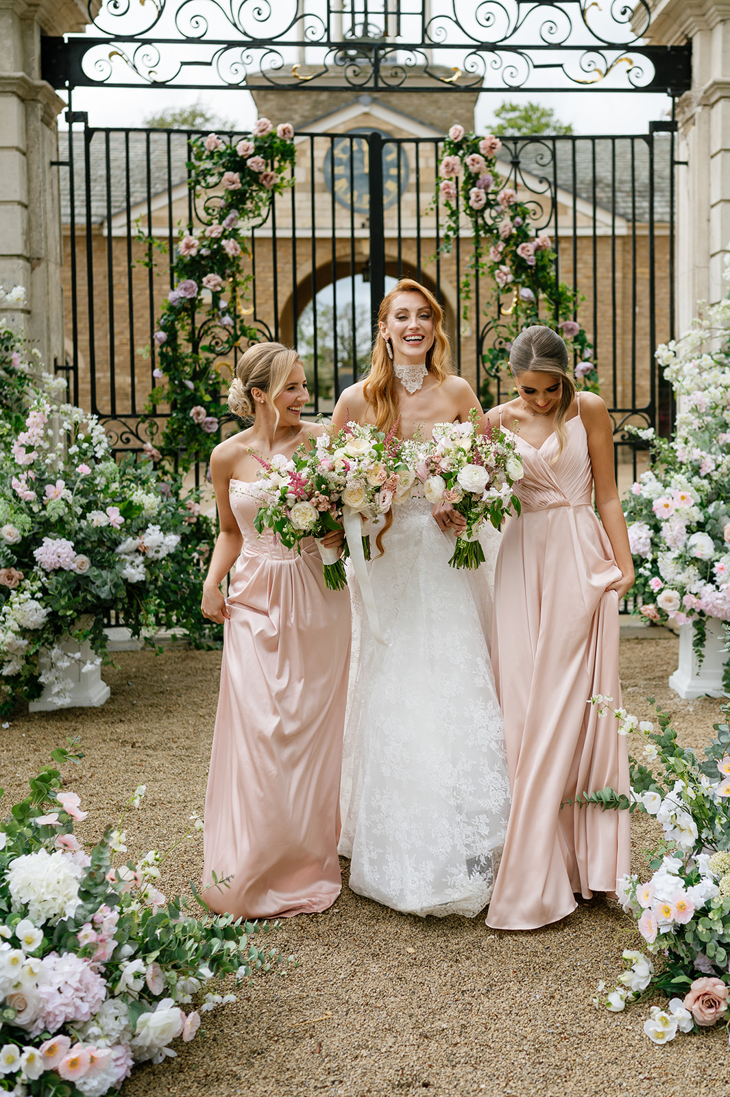 Bride laughing between two bridesmaids in blush satin gowns.