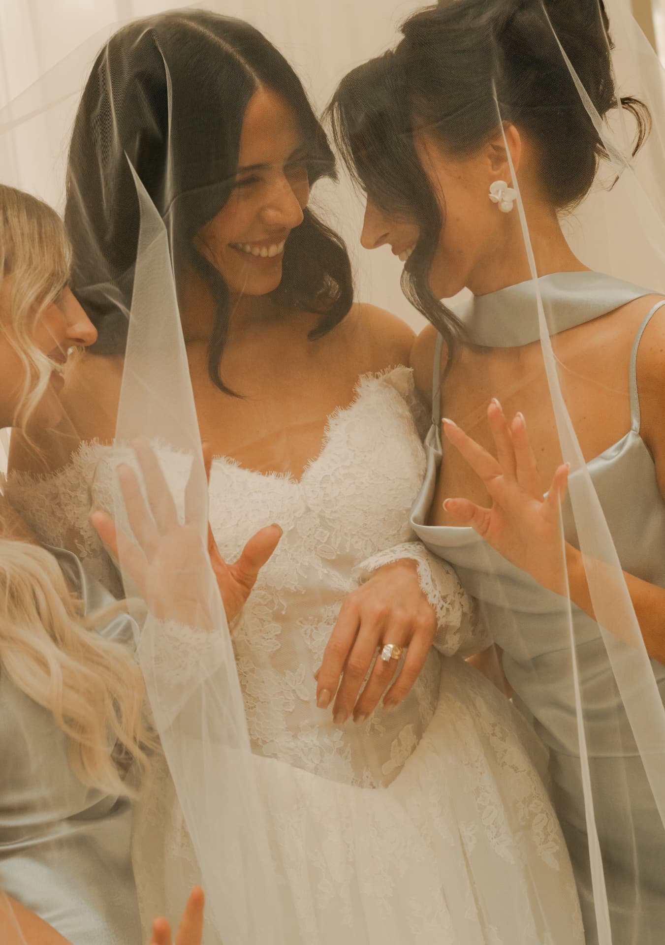Bride and bridesmaid smiling together beneath a veil.