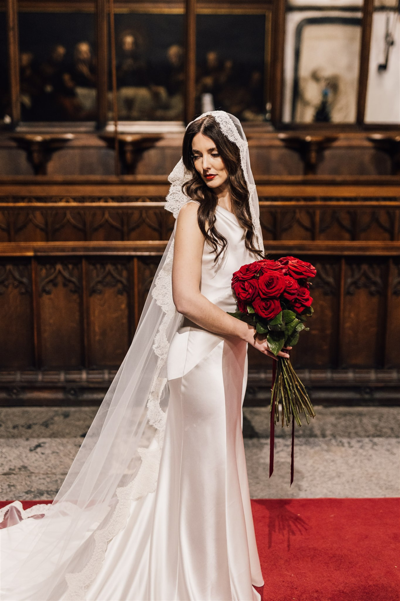 Bride holding red roses, looking down, inside Hull Minster.