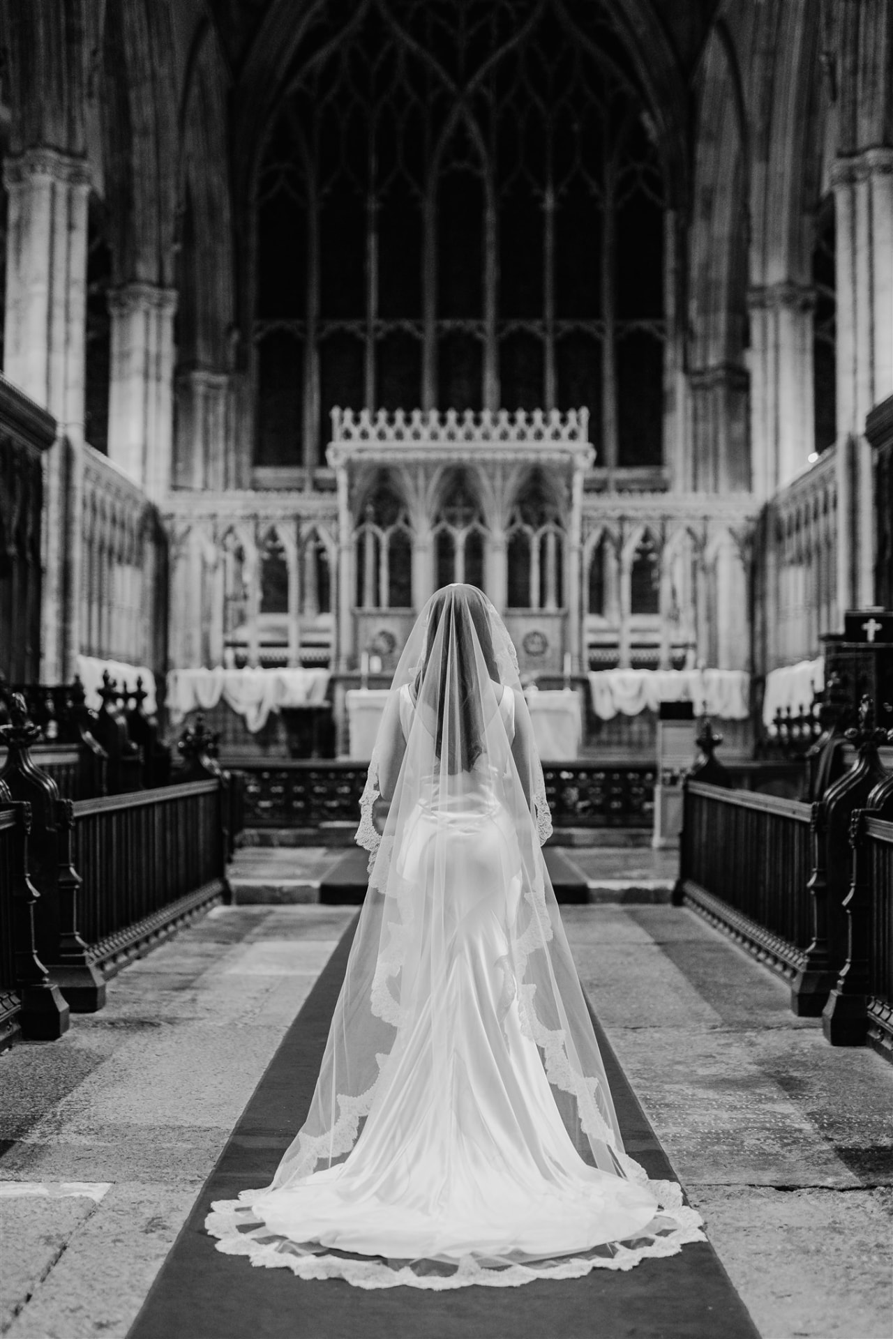 Black and white image of the bride from behind, walking towards the church altar.
