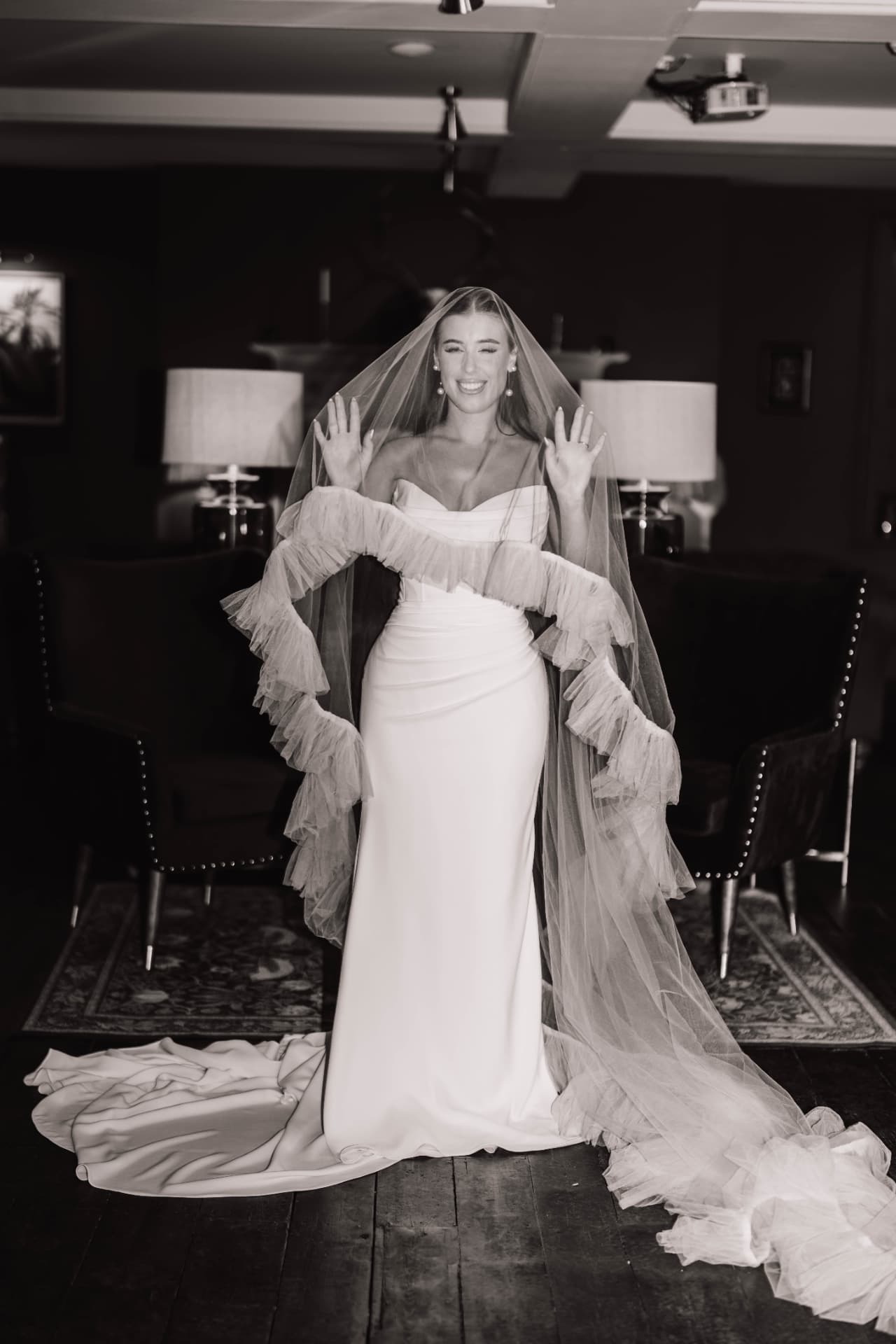 Bride smiling beneath a soft ruffled white veil.