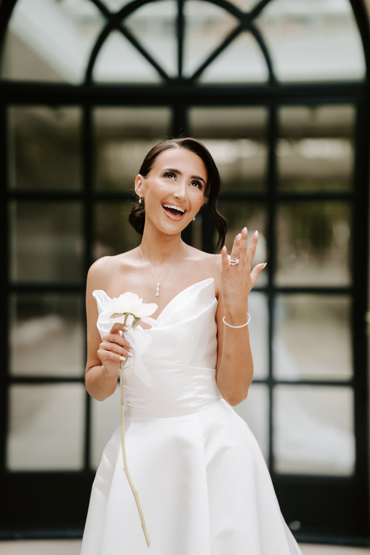 Bride laughing as she shows her ring, holding a single peony.