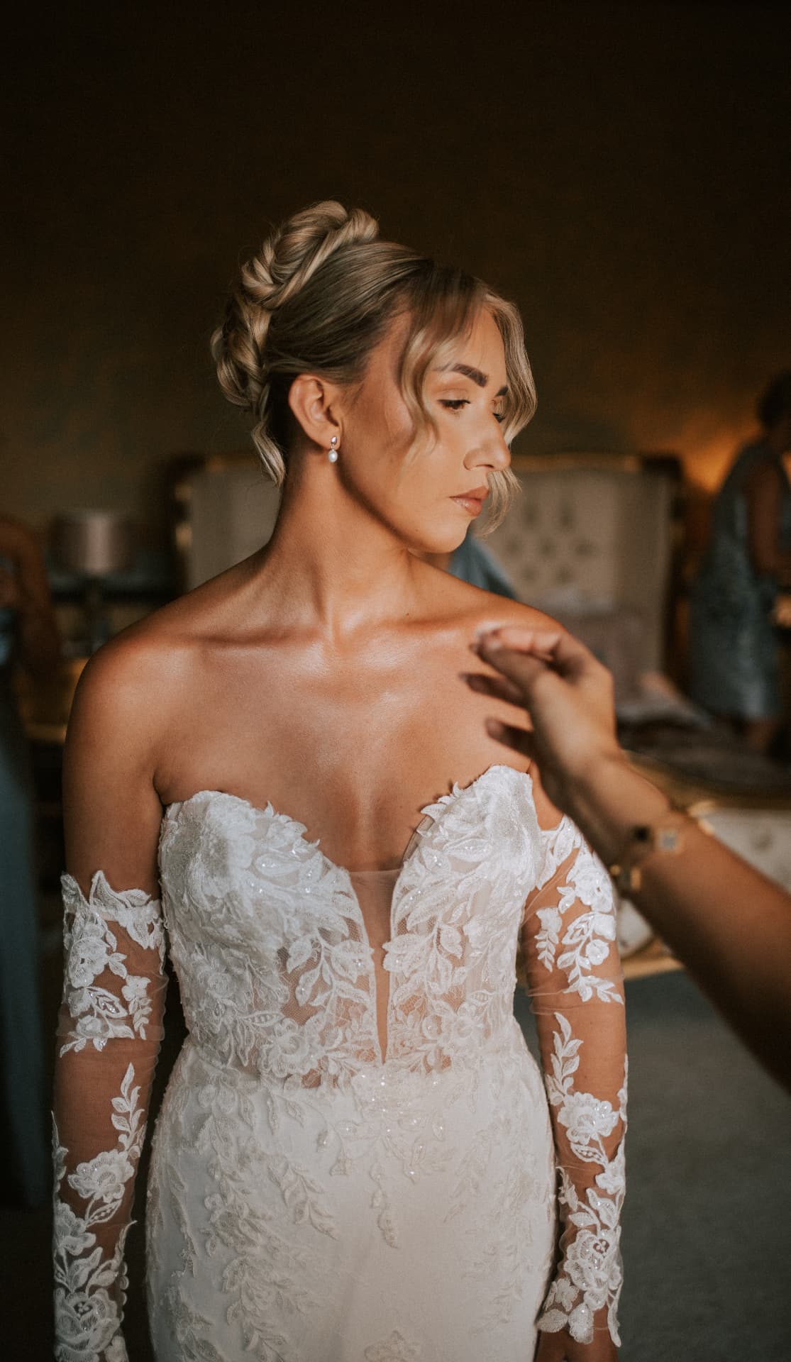 Bride with a polished braided updo wearing a strapless lace wedding dress with long lace sleeves.