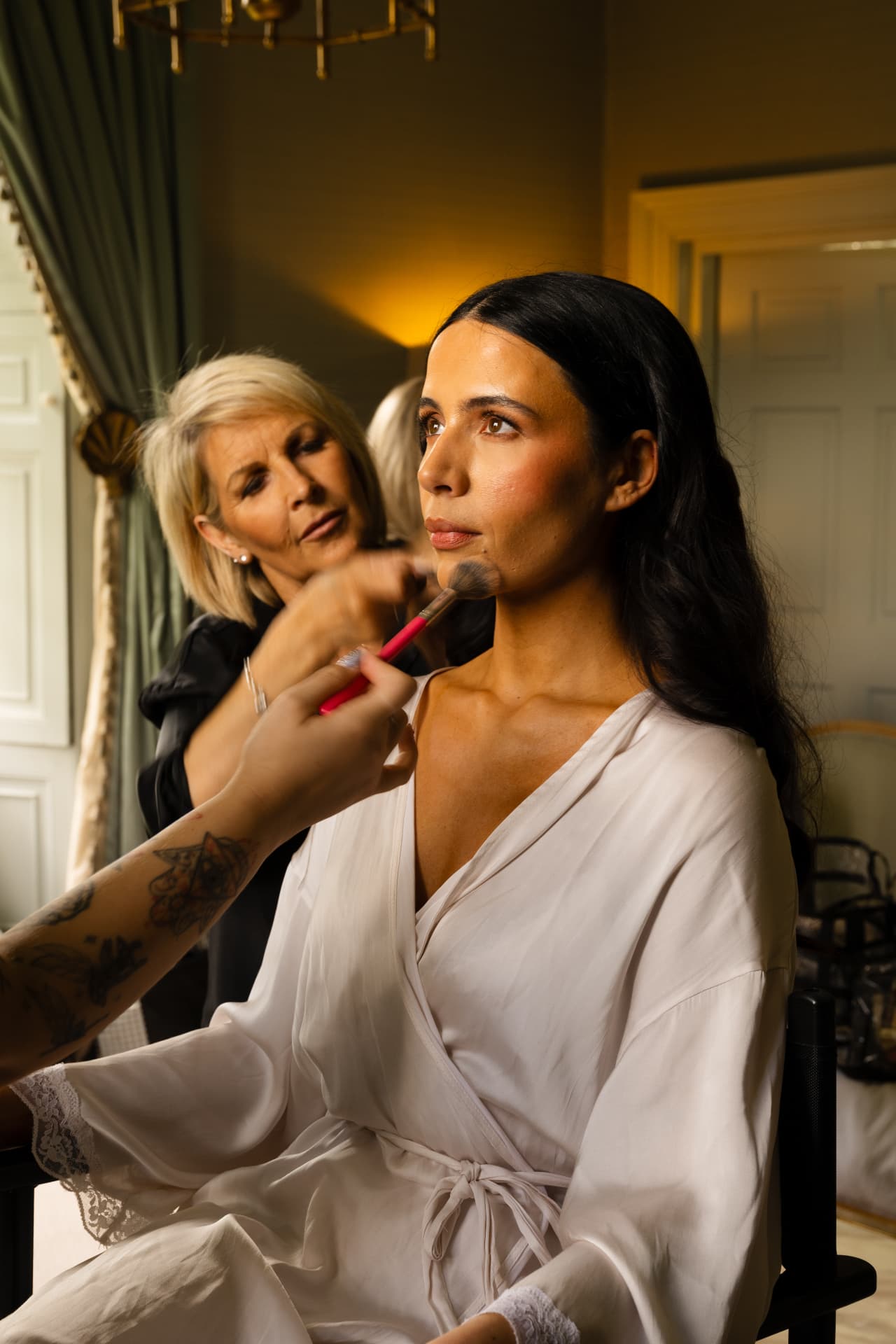 Bride having her make-up finished in a warmly lit dressing room.