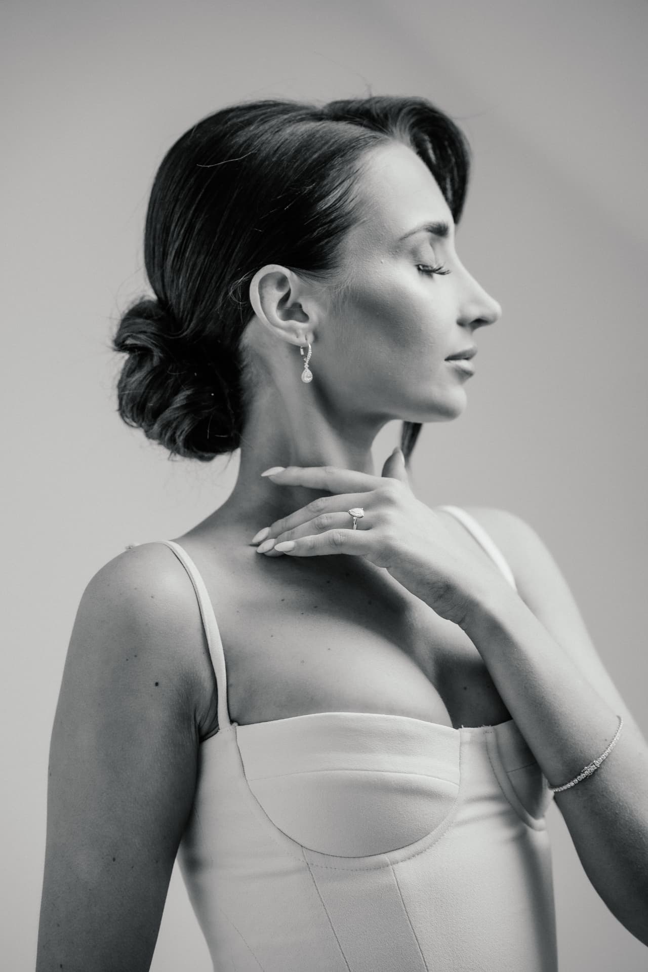 Black and white profile of a bride with a sculpted low bun, eyes closed and a hand at her chest.